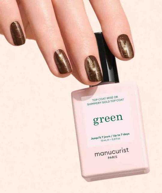 Top Coat Irisé Or GREEN™ Manucurist, manucure marron avec voile doré pailleté et flacon sur fond beige naturel