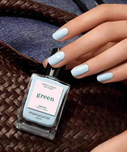 Manucurist Green Light Blue nail polish bottle with a pastel blue manicure in a natural summer setting.