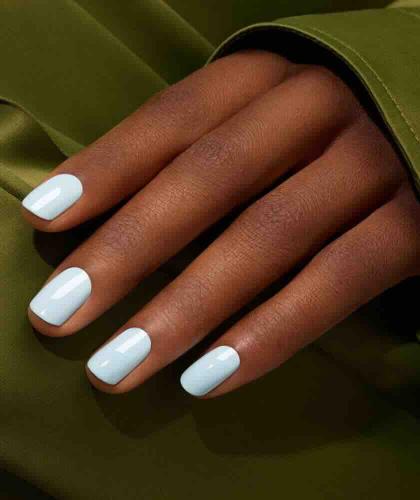 Gros plan sur des ongles bleu ciel pastel avec le vernis Green Light Blue de Manucurist, sur un tissu vert satiné.