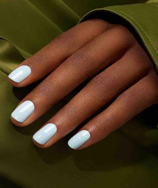Gros plan sur des ongles bleu ciel pastel avec le vernis Green Light Blue de Manucurist, sur un tissu vert satiné.