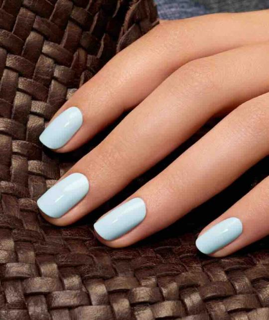 Gros plan sur des ongles bleu ciel pastel vernis avec Green Light Blue de Manucurist, ambiance naturelle et lumineuse.