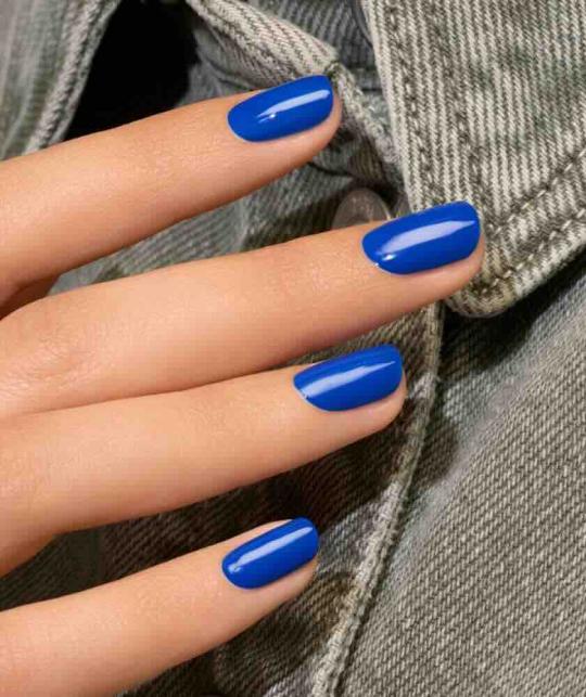 Ongles bleu électrique avec le vernis Ultramarine Manucurist sur un fond jean délavé dans une ambiance moderne.