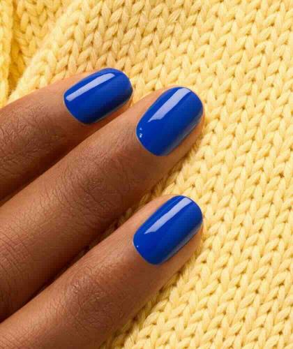 Ongles bleu électrique avec le vernis Ultramarine Manucurist mis en valeur sur une texture jaune en maille.
