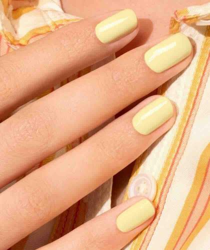 Pastel yellow manicure with Manucurist Mimosa nail polish, hands wearing a striped shirt for an elegant summer look.