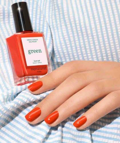Coral Reef Manucurist manicure with the coral nail polish bottle placed on a bright striped summer shirt.