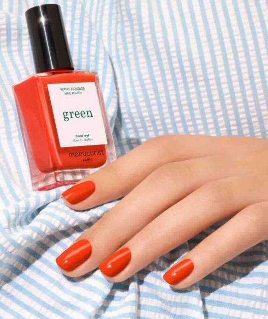 Coral Reef Manucurist manicure with the coral nail polish bottle placed on a bright striped summer shirt.
