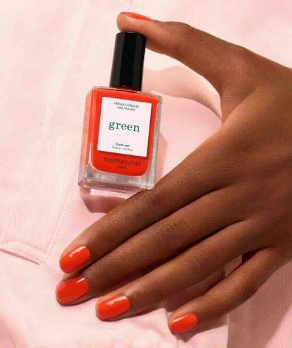 Coral Reef Manucurist manicure on tanned skin with the coral nail polish bottle on a pale pink background.
