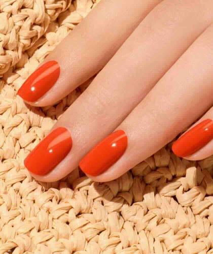 Close-up of a Coral Reef Manucurist manicure, a vibrant coral shade on a natural woven background.