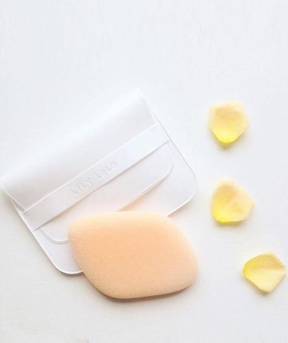 Éponge de maquillage Flocked Sponge LILY LOLO et pochette de rangement sur fond gris avec pétales jaunes