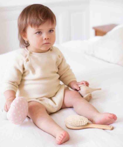 Baby sitting on a bed with the BACHCA Paris Baby Care Hair Brush