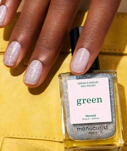 Hand holding a bottle of Mermaid Manucurist Green nail polish with shimmering holographic reflections