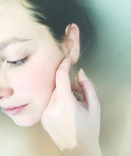 Frau mit strahlendem Teint, umgeben von Wasser – Joveda ayurvedische Hautpflege Made in India