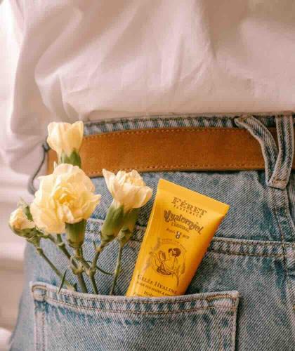 Hyalomiel Parfum Rose Poudrée Féret Parfumeur dans la poche d’un jean avec une fleur jaune